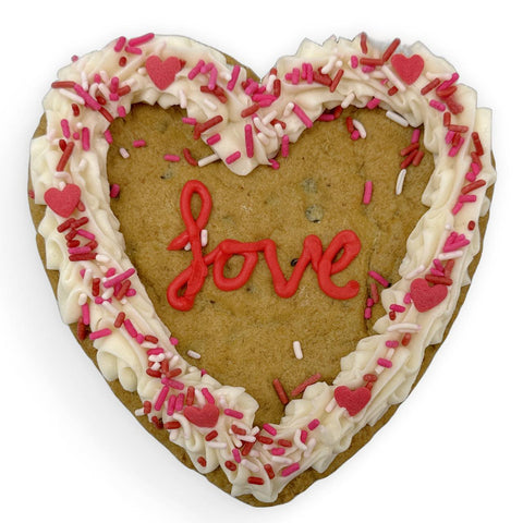 Gluten-free, dairy-free heart-shaped cookie cake with buttercream frosting, festive sprinkles, and a piped “love” message.